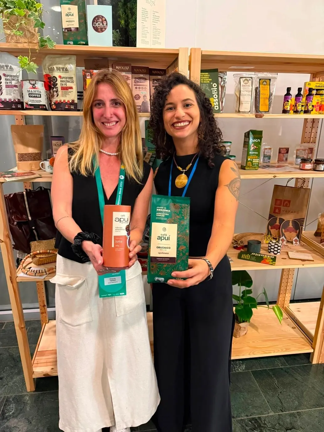 Two women holding packs of Café Apuí coffee in a shop with wooden shelves