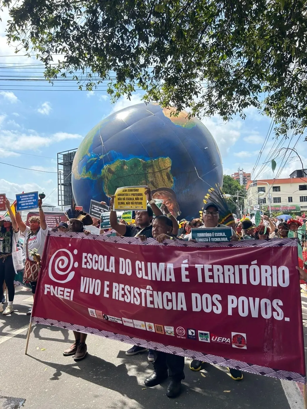 Demonstrationszug in Belém mit einem großen Weltkugel-Ballon und dem Transparent „Escola do clima é território vivo e resistência dos povos“