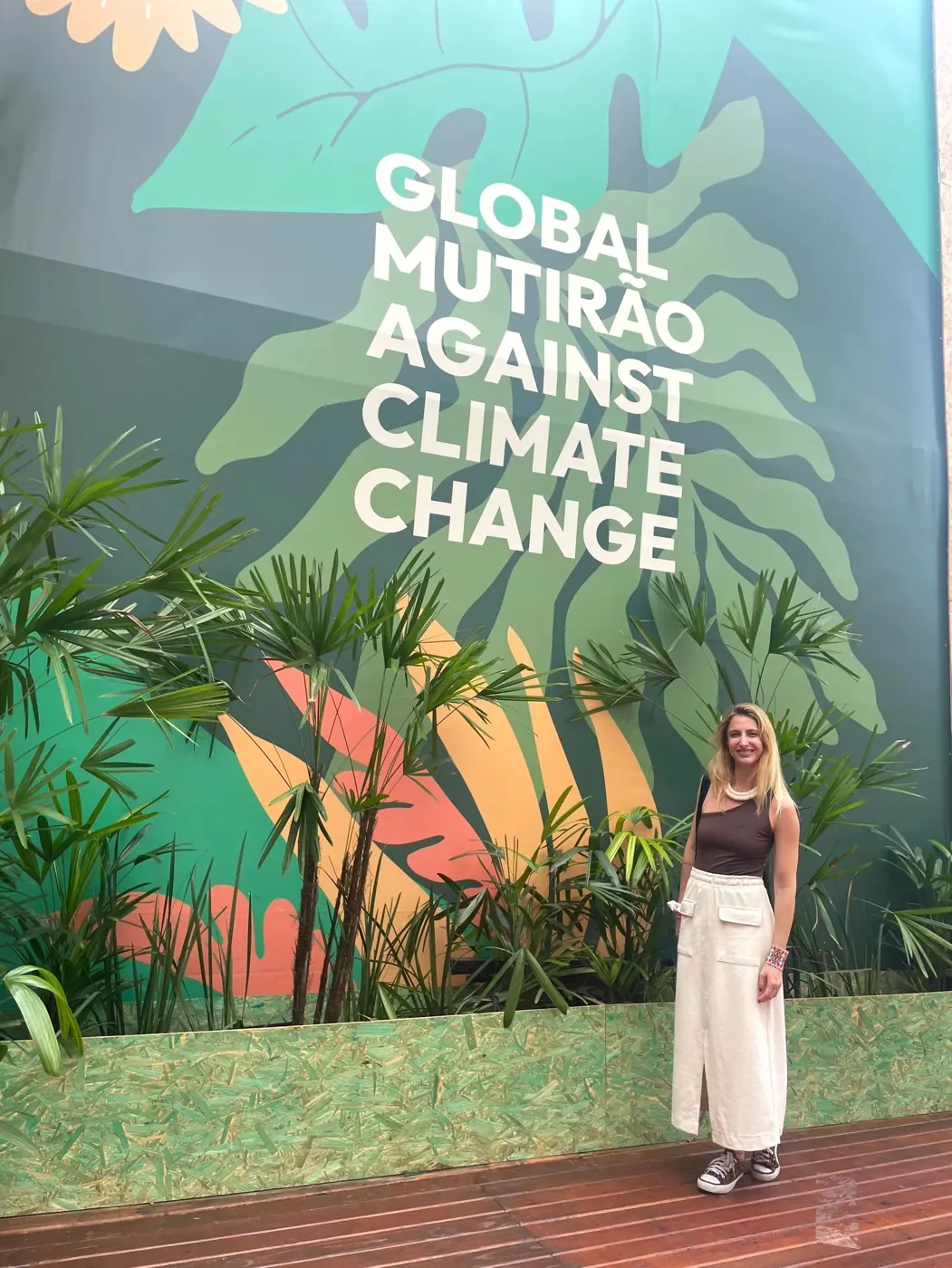 Priscila vor einer großen Wand mit der Aufschrift „Global Mutirão against Climate Change“