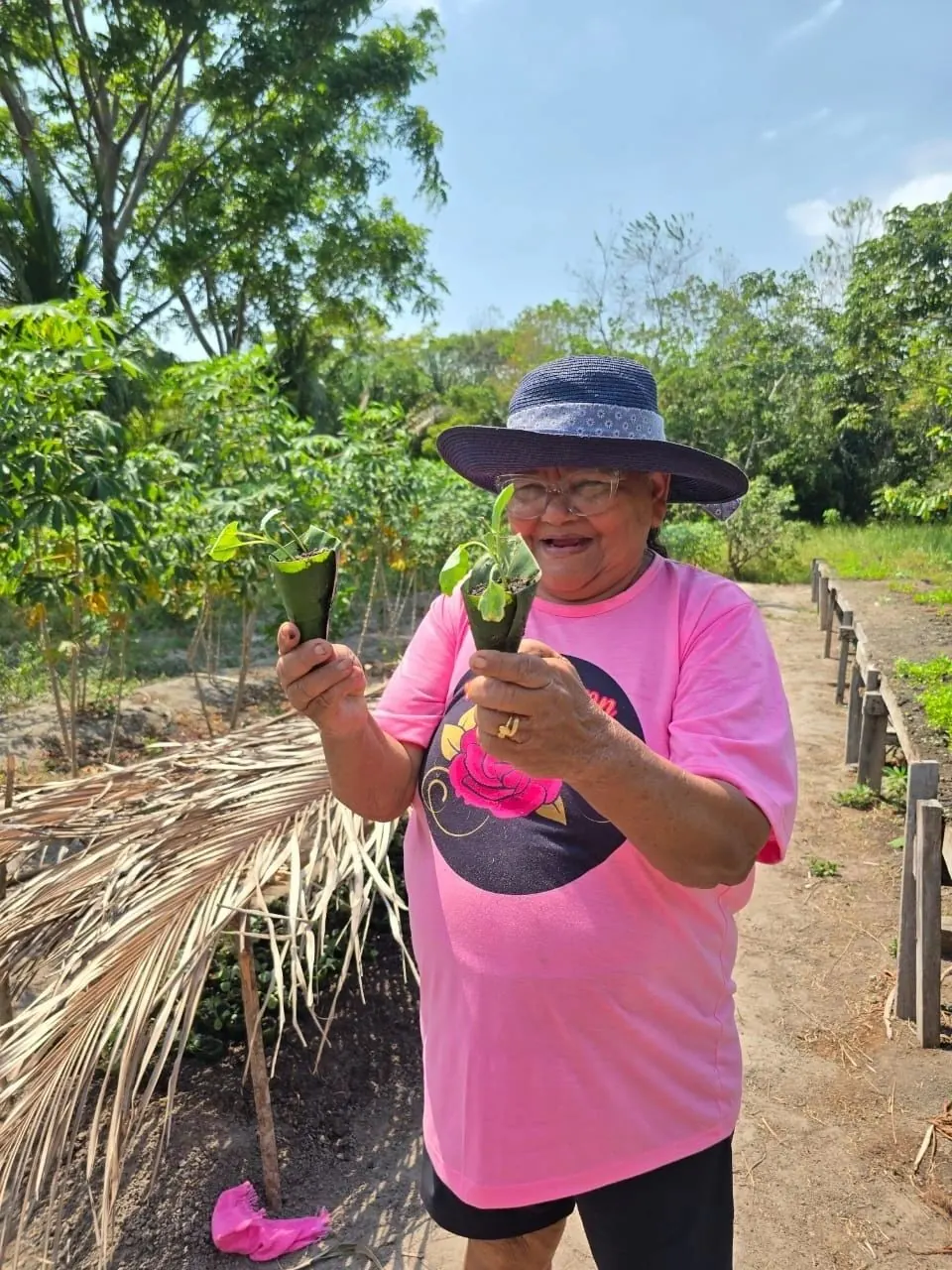 Dona Oneca mit Sonnenhut hält Setzlinge in ihrem Garten