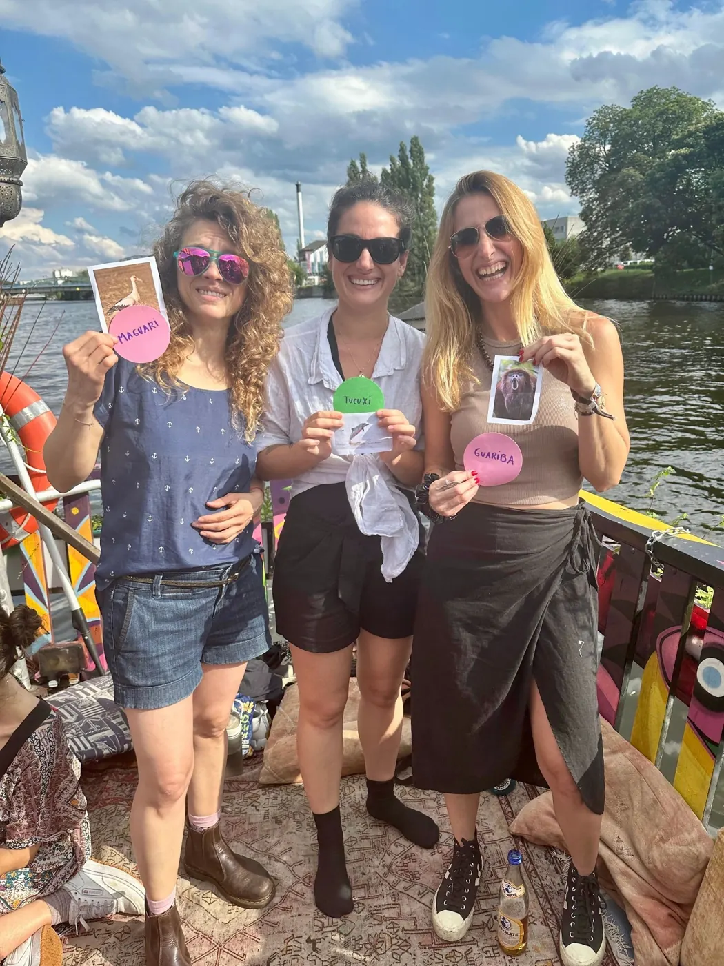 Drei Frauen an Deck eines Boots auf der Spree halten Spielkarten mit Tierbildern